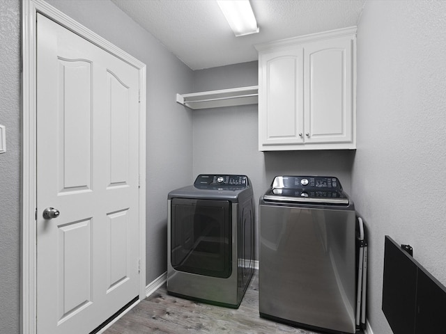 laundry area with cabinets, a textured ceiling, light wood-type flooring, and washer and clothes dryer