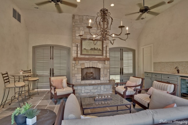 living room with a stone fireplace, high vaulted ceiling, sink, and ceiling fan with notable chandelier