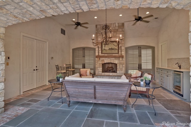 tiled living room with a stone fireplace, beverage cooler, brick ceiling, ceiling fan with notable chandelier, and sink