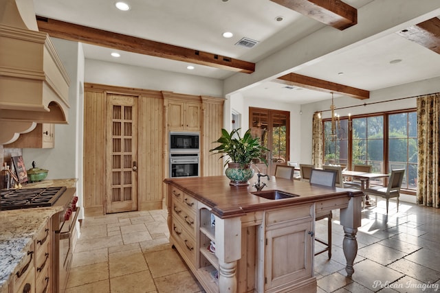 kitchen with stainless steel appliances, beamed ceiling, light tile floors, and light brown cabinets