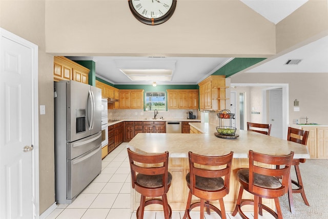 kitchen featuring light tile patterned floors, tasteful backsplash, a kitchen bar, kitchen peninsula, and stainless steel appliances