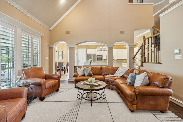 living room with an inviting chandelier, high vaulted ceiling, crown molding, and ornate columns