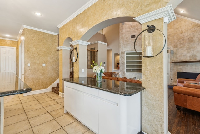 kitchen featuring ornate columns, dark stone countertops, white cabinetry, and ornamental molding