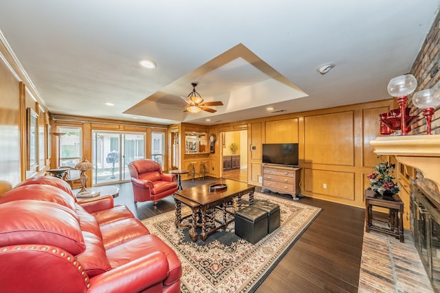 living room with a raised ceiling, ceiling fan, and wood-type flooring