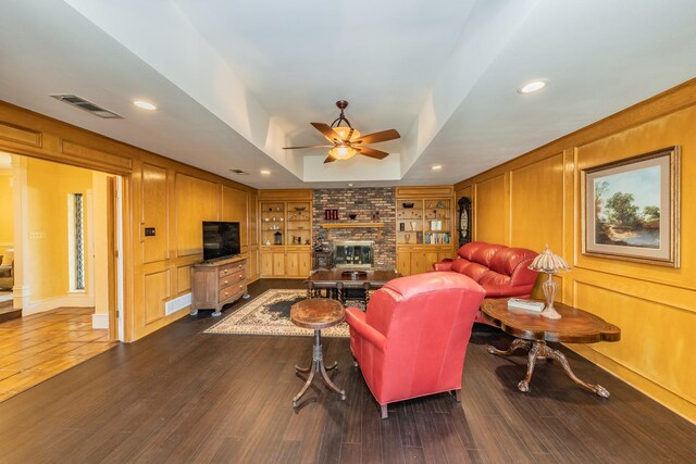 living room featuring brick wall, dark hardwood / wood-style floors, a brick fireplace, ceiling fan, and a raised ceiling