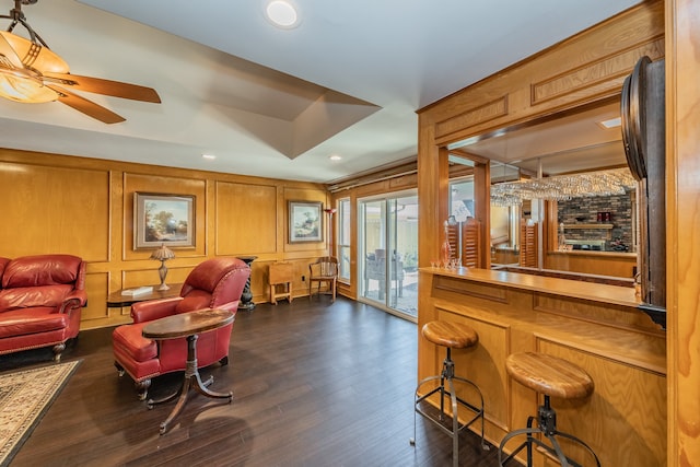 living room with ceiling fan, wood walls, and dark wood-type flooring