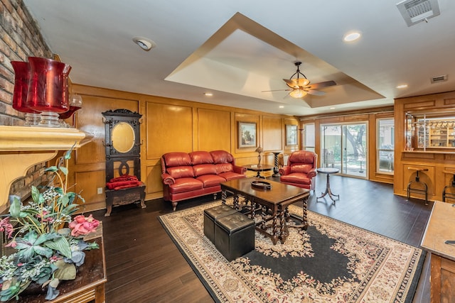 living room featuring dark wood-type flooring, ceiling fan, and a raised ceiling