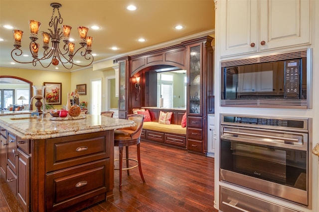 kitchen with black microwave, stainless steel oven, sink, an inviting chandelier, and an island with sink