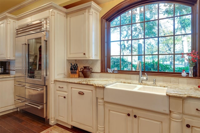 kitchen with backsplash, dark wood-type flooring, stainless steel built in fridge, sink, and light stone counters