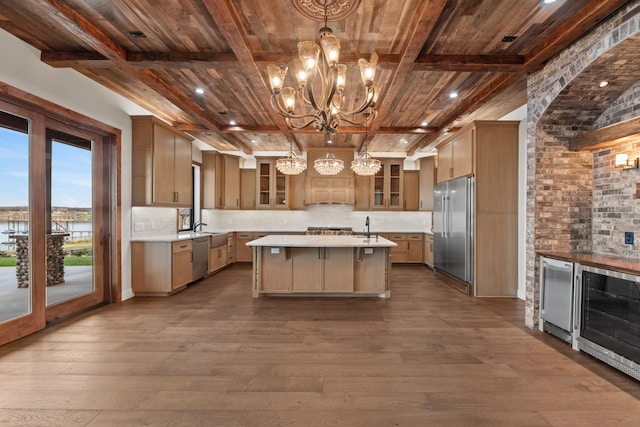 kitchen featuring beamed ceiling, a kitchen island with sink, decorative light fixtures, dark wood-type flooring, and stainless steel appliances