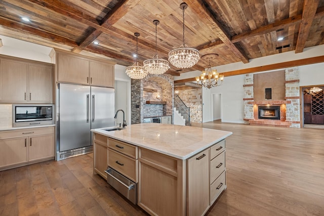kitchen featuring a stone fireplace, hardwood / wood-style floors, a sink, built in appliances, and a notable chandelier