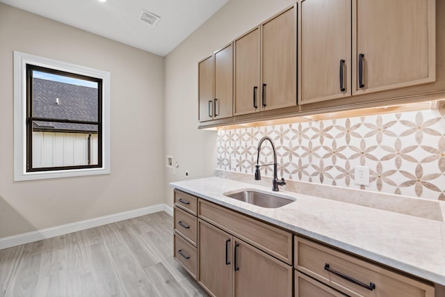 kitchen with light brown cabinets, sink, backsplash, light stone counters, and light hardwood / wood-style flooring