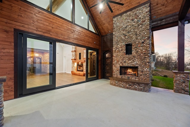 patio terrace at dusk featuring ceiling fan and an outdoor stone fireplace