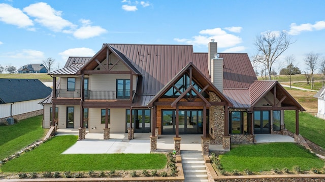 back of property featuring a patio area, metal roof, a lawn, a chimney, and a balcony