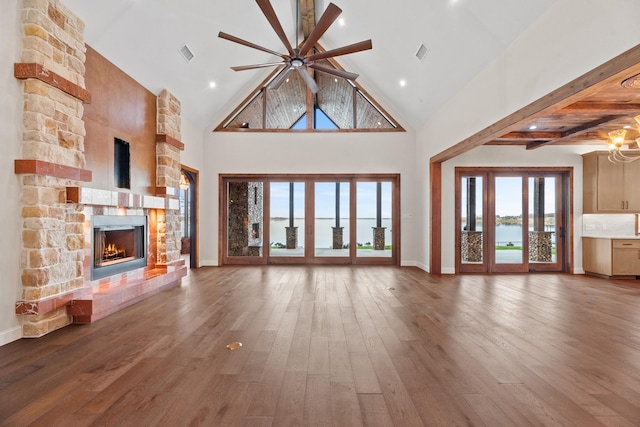 unfurnished living room with hardwood / wood-style flooring, a fireplace, ceiling fan with notable chandelier, high vaulted ceiling, and beamed ceiling