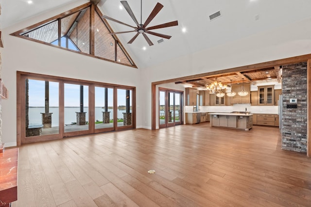 unfurnished living room with light wood-type flooring, a water view, a high ceiling, ceiling fan with notable chandelier, and beamed ceiling