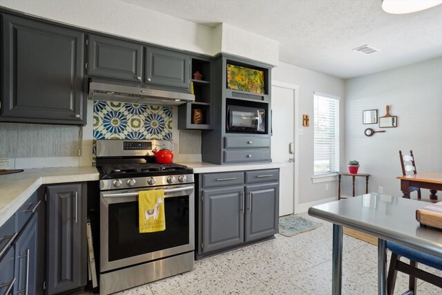 kitchen featuring stainless steel gas range oven, built in microwave, a textured ceiling, and light tile floors