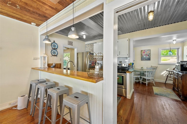 kitchen with dark wood-style flooring, a breakfast bar area, butcher block counters, hanging light fixtures, and appliances with stainless steel finishes