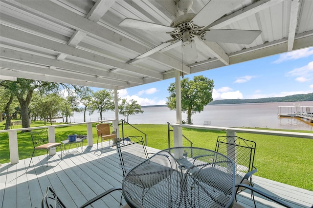 wooden terrace featuring a water view, ceiling fan, a lawn, and outdoor dining space