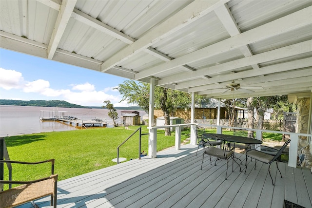 wooden deck with a water view, a ceiling fan, and a yard