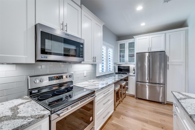 kitchen featuring white cabinetry, light stone countertops, tasteful backsplash, light hardwood / wood-style flooring, and appliances with stainless steel finishes