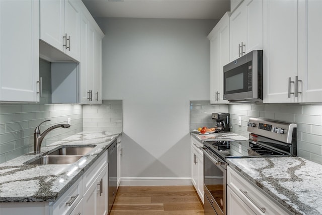 kitchen featuring light stone countertops, backsplash, stainless steel appliances, sink, and white cabinetry