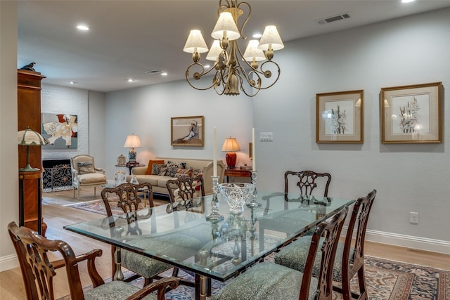 dining room with a large fireplace, an inviting chandelier, and light hardwood / wood-style flooring