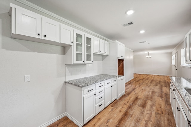 kitchen with tasteful backsplash, light stone countertops, white cabinets, and light wood-type flooring