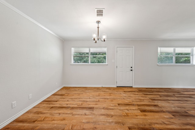 empty room featuring crown molding, an inviting chandelier, and light wood-type flooring