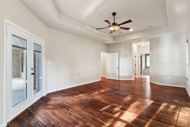 empty room with ceiling fan, french doors, a raised ceiling, and dark hardwood / wood-style floors