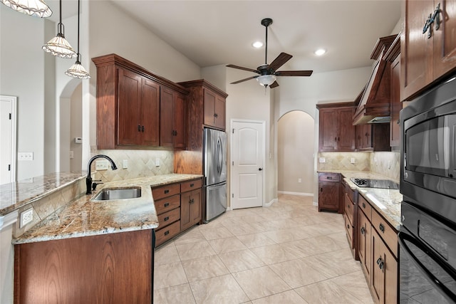 kitchen featuring sink, light stone counters, hanging light fixtures, and stainless steel fridge