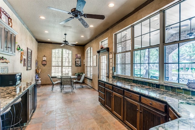 kitchen featuring dark stone countertops, ceiling fan, ornamental molding, dark brown cabinetry, and a textured ceiling