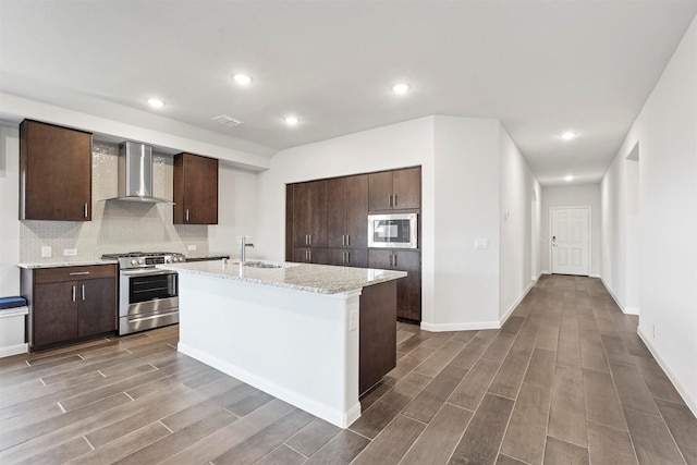 kitchen featuring a center island with sink, stainless steel range with gas cooktop, sink, wall chimney exhaust hood, and built in microwave