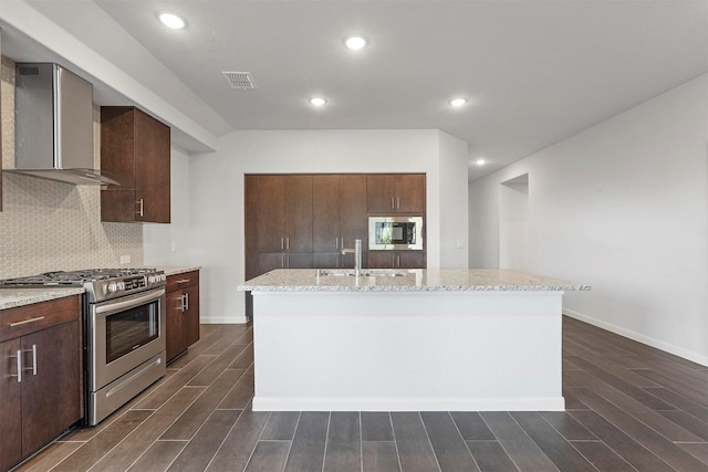 kitchen with decorative backsplash, appliances with stainless steel finishes, sink, wall chimney range hood, and an island with sink