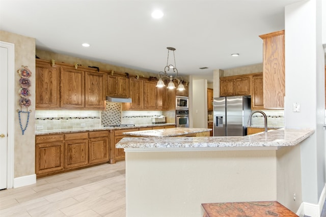 kitchen with an inviting chandelier, hanging light fixtures, appliances with stainless steel finishes, light stone counters, and kitchen peninsula