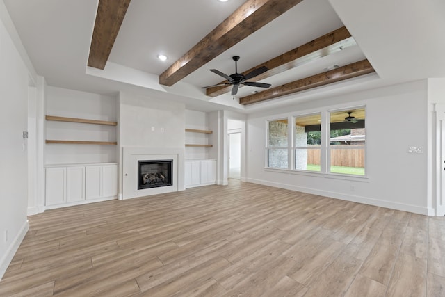 unfurnished living room with built in shelves, light wood-type flooring, and a tray ceiling