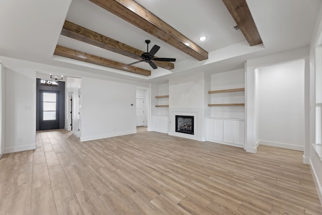 unfurnished living room featuring built in shelves, light wood-type flooring, a tray ceiling, and ceiling fan with notable chandelier