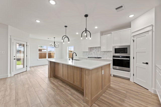 kitchen with a chandelier, stainless steel oven, white cabinets, and a kitchen island with sink