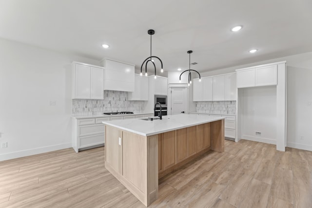 kitchen featuring gas stovetop, pendant lighting, white cabinets, and a kitchen island with sink