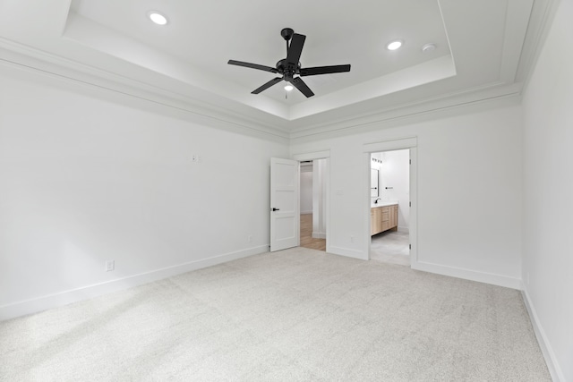 unfurnished bedroom with ceiling fan, a tray ceiling, ensuite bath, and light carpet