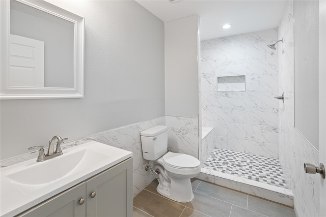 bathroom featuring tile flooring, tiled shower, tile walls, toilet, and large vanity