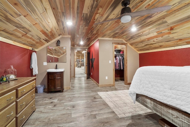 bedroom with a closet, a walk in closet, light wood-type flooring, wood ceiling, and sink