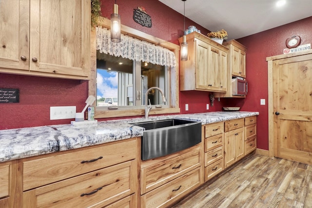 kitchen featuring decorative light fixtures, sink, light stone countertops, and light wood-type flooring