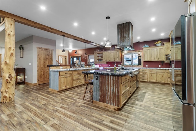 kitchen with wall chimney range hood, a center island with sink, a breakfast bar, and hardwood / wood-style flooring