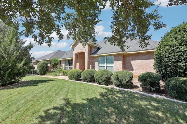 view of front facade with a shingled roof, a front lawn, and brick siding