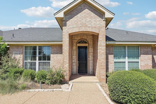 property entrance featuring brick siding and roof with shingles