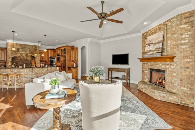 living room featuring a large fireplace, dark hardwood / wood-style floors, ceiling fan, and ornamental molding