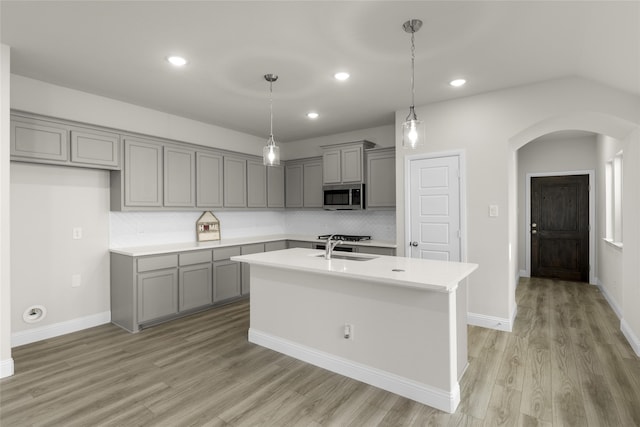 kitchen featuring decorative backsplash, a kitchen island with sink, hanging light fixtures, gray cabinetry, and light wood-type flooring