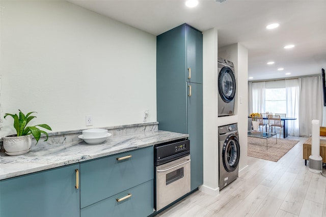 kitchen with light stone counters, stacked washer / drying machine, oven, and blue cabinetry