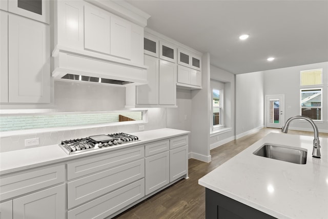kitchen with a sink, stainless steel gas cooktop, backsplash, glass insert cabinets, and white cabinets